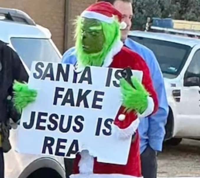 The Worst Human In The World Dressed Up As The Grinch Outside Of An Elementary School With A Sign That Said That Santa Is Fake
